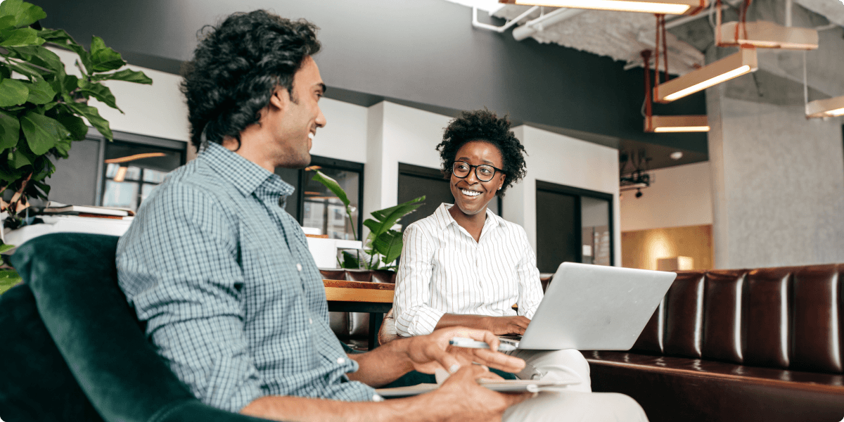 Two people smile in a casual office lounge, while working.